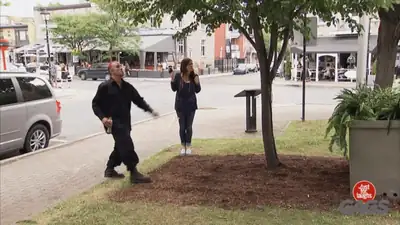 Man in black clothes walking past a woman in a polka dot top who is startled and looking up, on a city street, from a Just For Laughs Gags clip